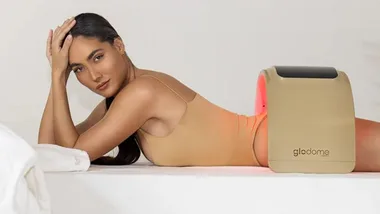 Model lying on her side using Glodome light therapy device on her lower back, wearing a beige outfit.