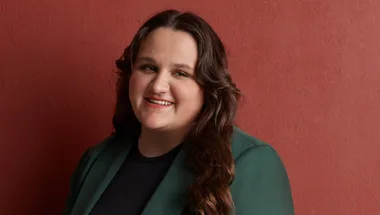 Sarah Williams CEO of What Were You Wearing Australia in a green suit against a dark red backdrop