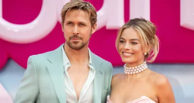 Actors in stylish attire pose together on a red carpet with a bright, bold pink background.