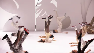 Dancers lying on stage with legs raised, wearing red-soled shoes.